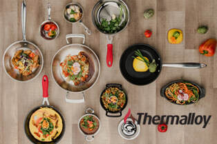 Collection of Thermalloy pans with food on a wood table. 